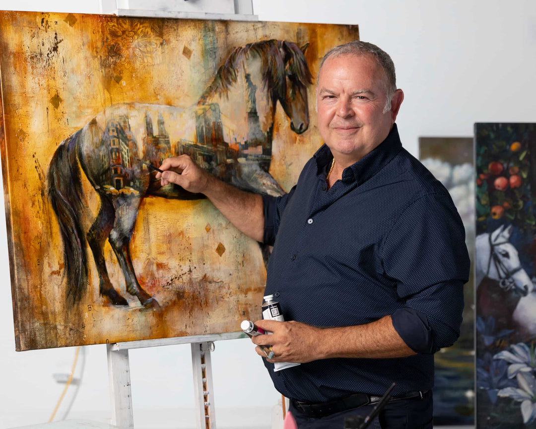 John turns and smiles at the camera while painting a horse