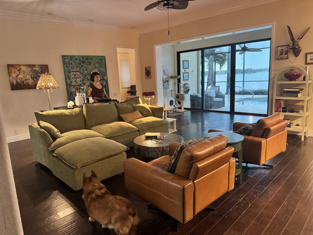 Elli Milan’s living room before the change, with an olive green sectional, two leather chairs, and the lake through sliding glass doors