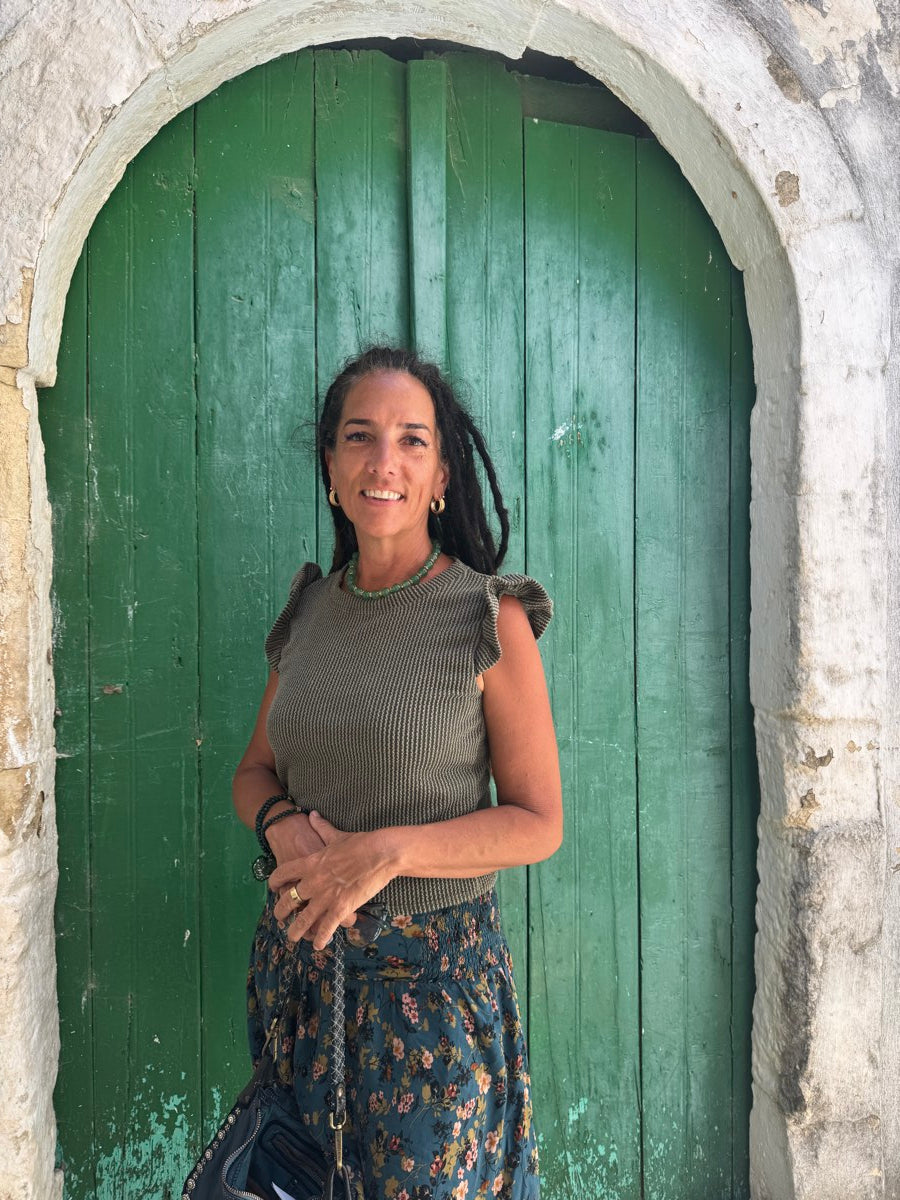 Elli Milan smiling in front of a weathered green door, wearing an emerald-toned necklace